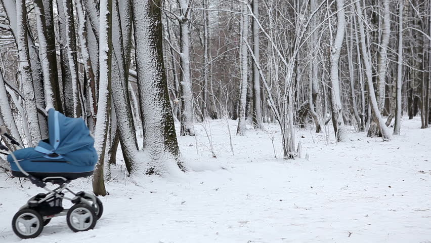 young woman walking with a baby carriage in winter park