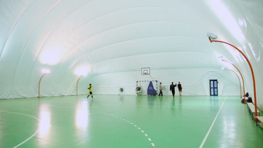 Four men play soccer on football field under cupola in inflatable gymnasium, panoramic motion