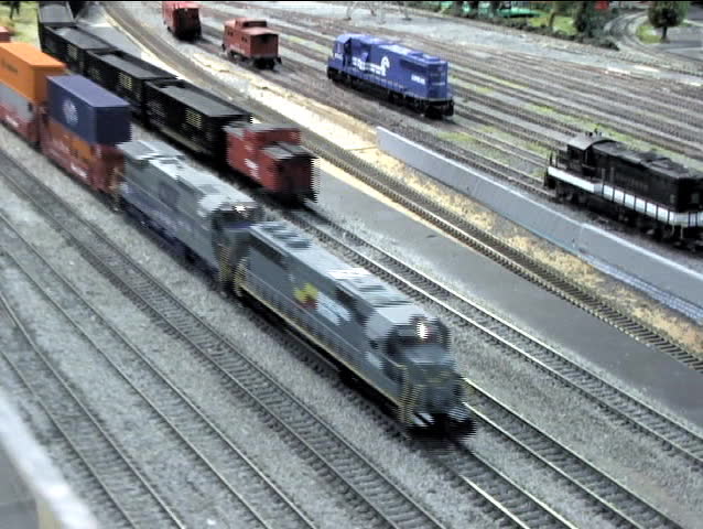 A long line of model railroad single and double stacked cars move and wobble on the track.