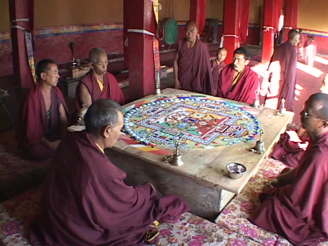 Buddhist monks sit and chant around a mandala.