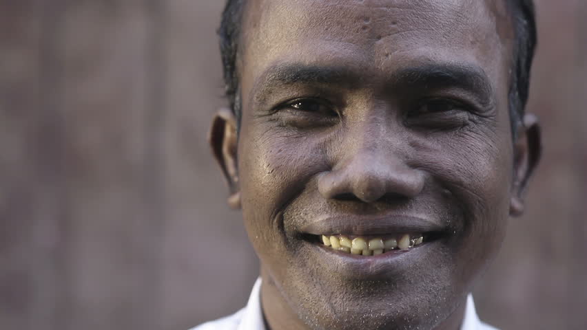 Portrait of mid adult asian man stepping into the frame and smiling at camera against brown wall. Close up