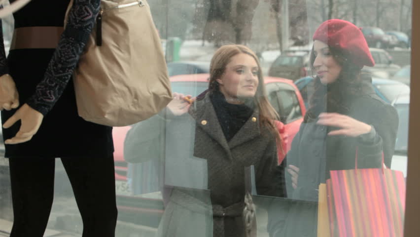 Two girls with shopping bags looking at the shopping window and discussing the outfit