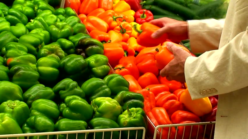 A man in the produce section looking over the colorful peppers.