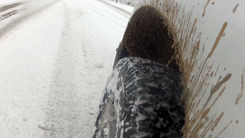 Truck tire drive in deep fresh snow blizzard on highway road in Fountain Green. Low view of tire with ice and mud. First person close view. 