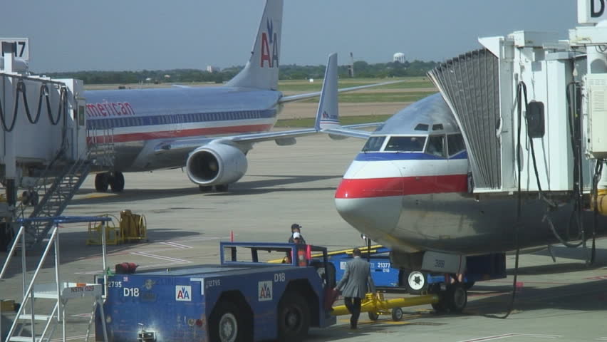 Airport workers ready plane at gate while another jet is pushed onto tarmac