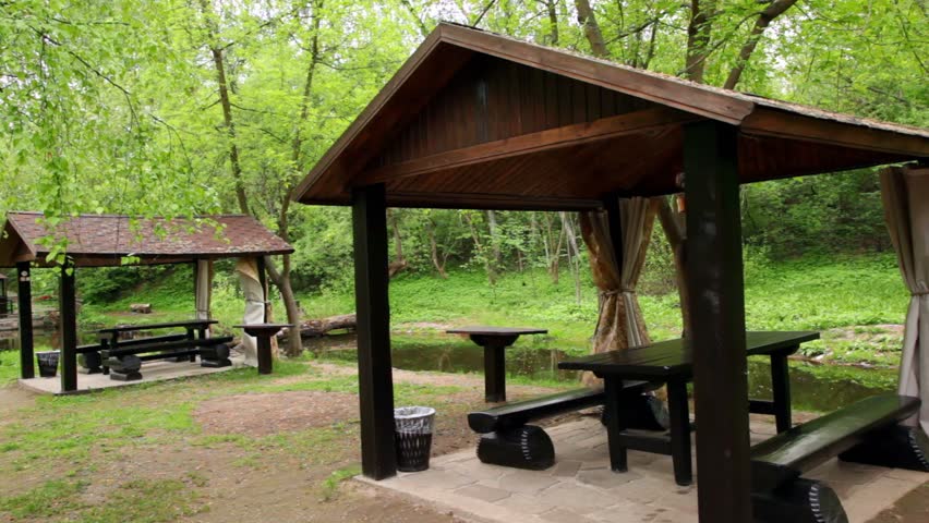 Three summerhouses ashore of small pond at among trees at summer, shown in motion
