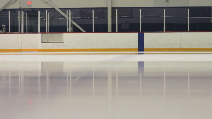 An ice making machine cruises by on the ice rink cleaning the surface for new skaters.