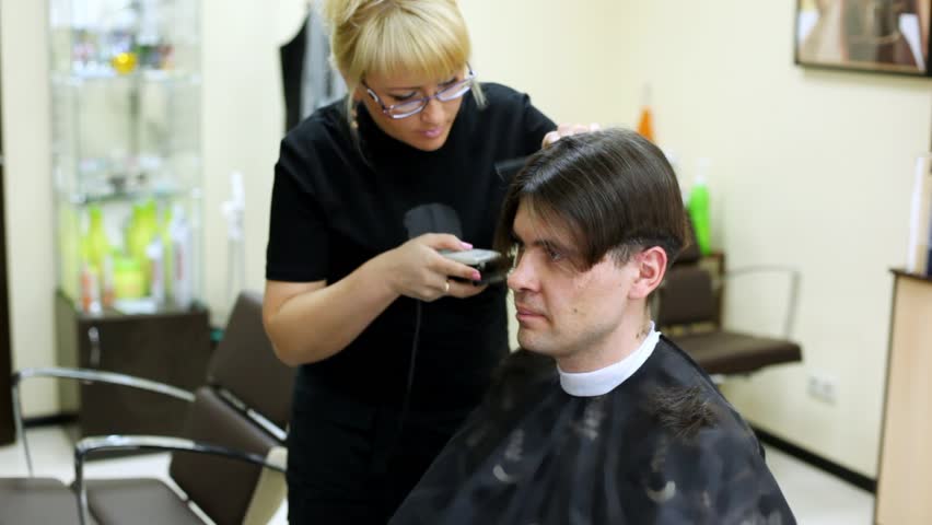 Hairdresser cuts hair to man to brunet with long hair
