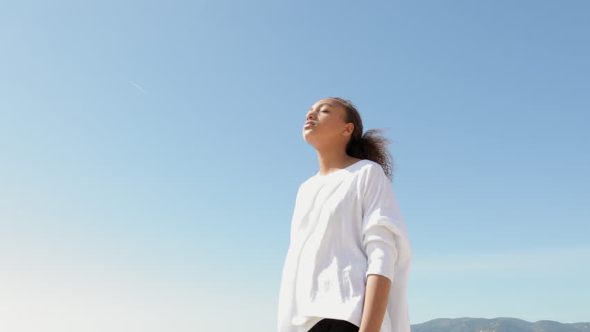 Girl stretching her arms in the air against a blue sky.