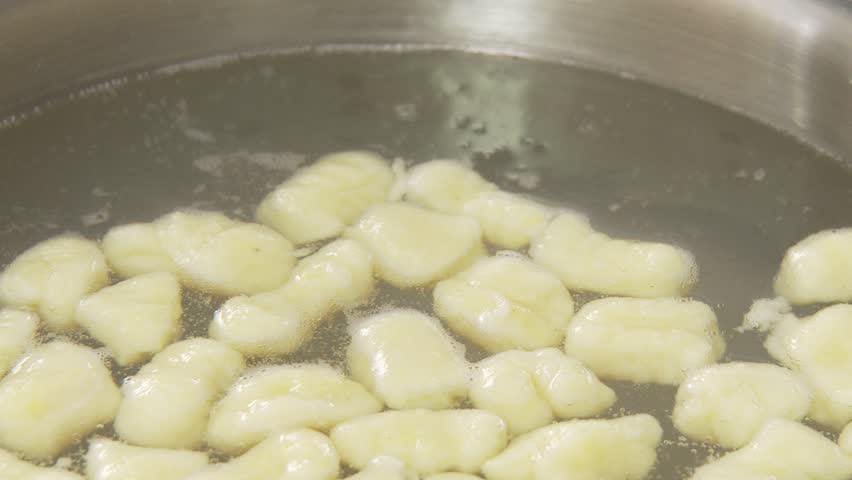 Gnocci being removed from salt water with a draining spoon