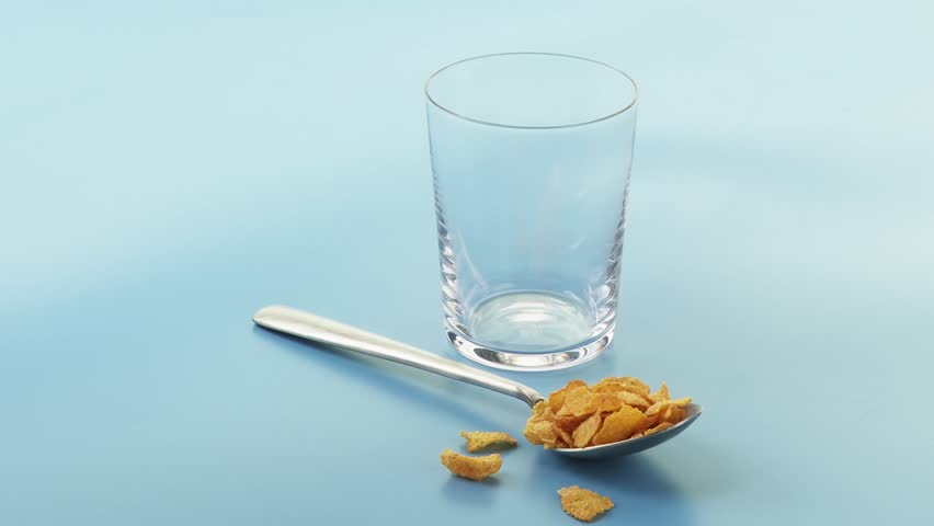 A spoonful of cornflakes and a glass of milk being poured