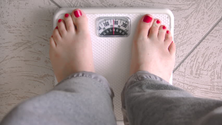 Female Standing on Weight Scale (HD). Female standing on a white generic weight scale to measure her pounds just shy of 180lbs.