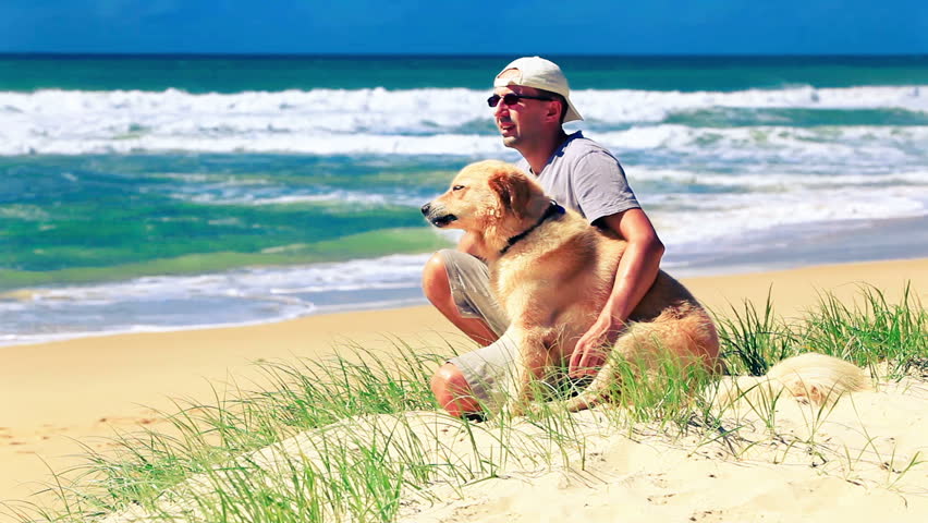 Male owner sitting on a beach with a dog