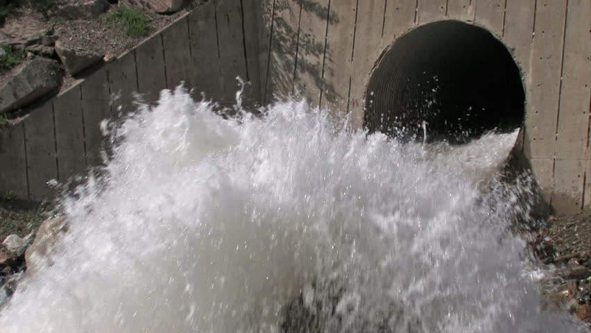 Violent flood water exiting concrete pipe. Fast moving and stained with mud and dirt. Wasatch Mountains above Salt Lake City, Utah.