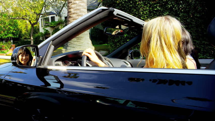 Beautiful girls singing and laughing in a luxury open top car