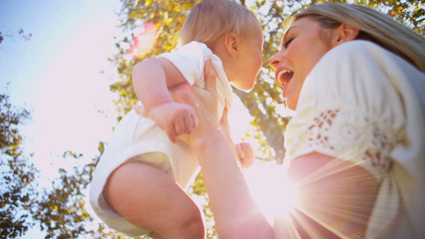 Beautiful blonde mother and baby exchange a tender kiss as they play together outdoors