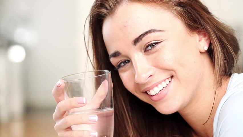 Pretty young girl is happy and cheerful as she drinks a glass of water to stay healthy