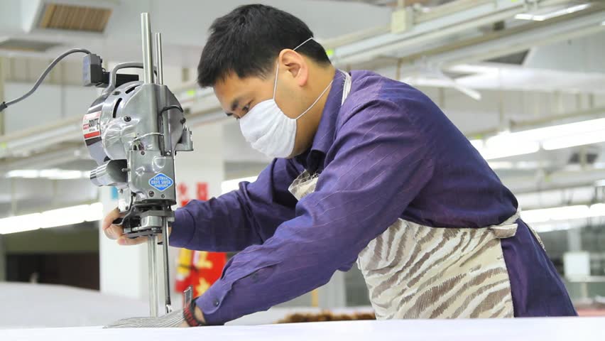 SHENZHEN, CHINA -  JUNE 5: male chinese textile factory worker cutting large pile of fabric. June 5, 2011 in Shenzhen, China