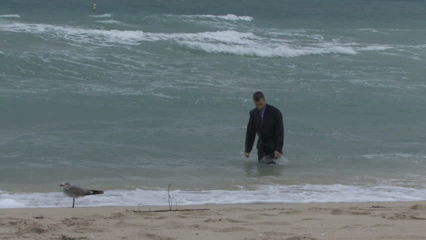 Male walking out of the ocean in suit with his head down