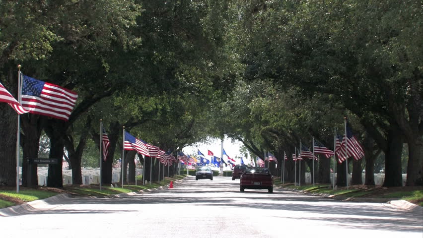 Graves and headstones at Ft Sam Houston Veterans Cemetery San Antonio Texas. Headstones and flags. Heroes and warriors, members of military and veterans. Entrance road and cars.