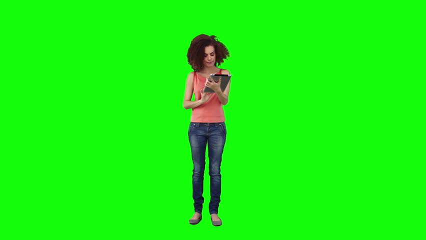 A brunette woman is using a tablet computer in front of a green background