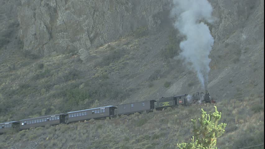 Steam Locomotive moves into Frame, scene is Engine comes into frame and traverses steep hill side belching smoke