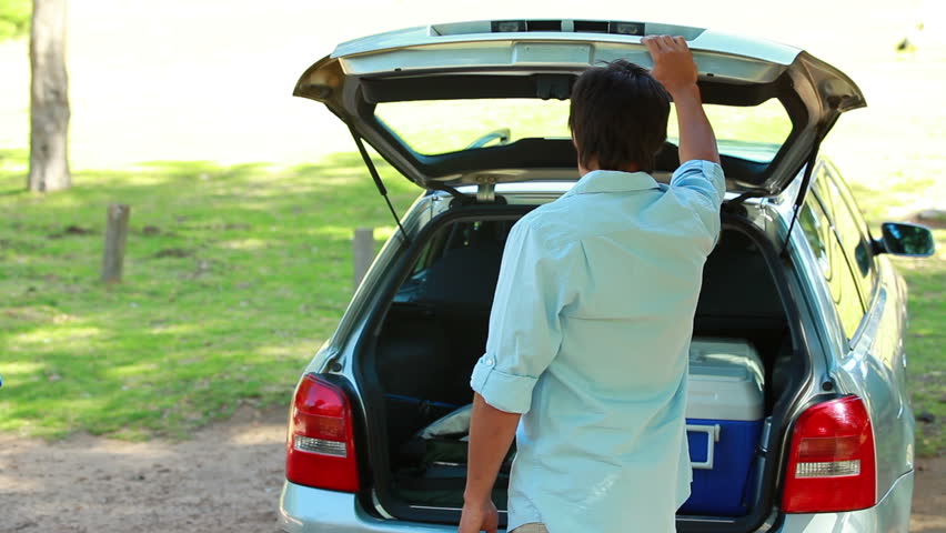 Father emptying the trunk of the car with his family on a parking