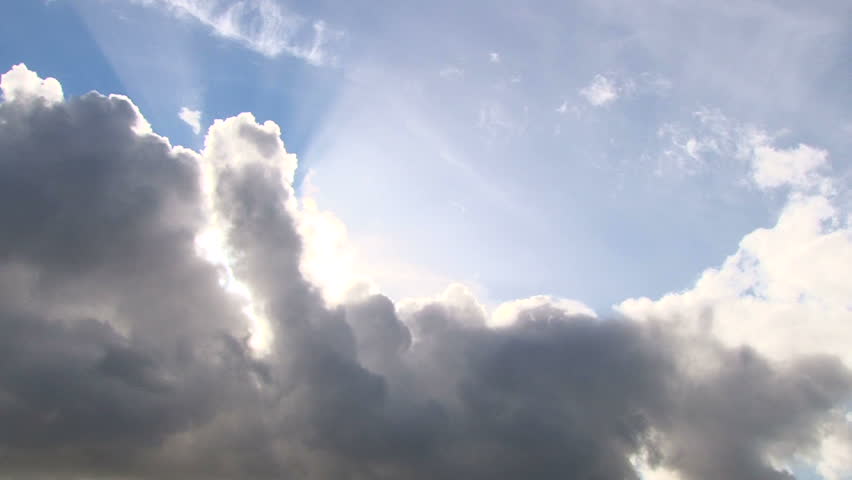 Beautiful cloudscape with large, building clouds and sunset behind shining sun rays and eventually breaking through cloud mass.