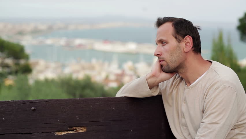 Young sad, depressed man sitting on bench, outdoors

