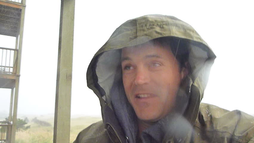 Man standing outside gets rained on and blown by heavy winds during rain storm.