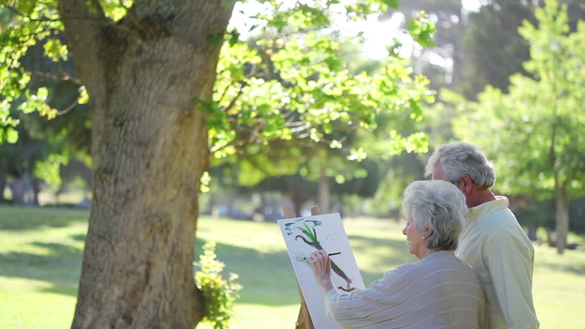 Mature couple painting trees in a park