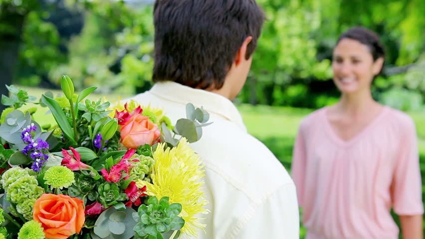 Smiling brunette woman receiving a bunch of flowers in a parkland