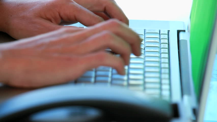 Close-up on hands typing on a keyboard and picking up the phone in a bright office