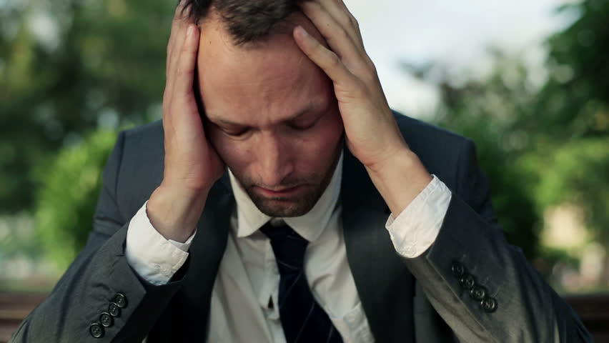 Depressed, sad young businessman sitting in the park, dolly shot
