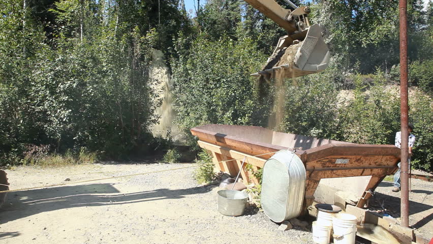 FAIRBANKS, ALASKA - CIRCA JUL 2010: Backhoe loading and dumping mineral rich dirt and rocks into a mining sluice box circa July 2010 in Fairbanks, Alaska. Water runs through to recover gold dust and nuggets.