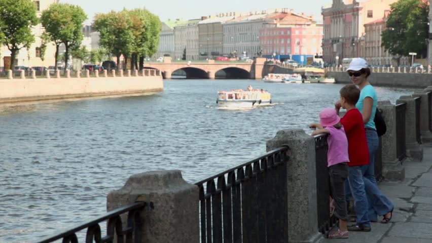 Mother in sunglasses with two her kids stand at quay and watch on ship float by river