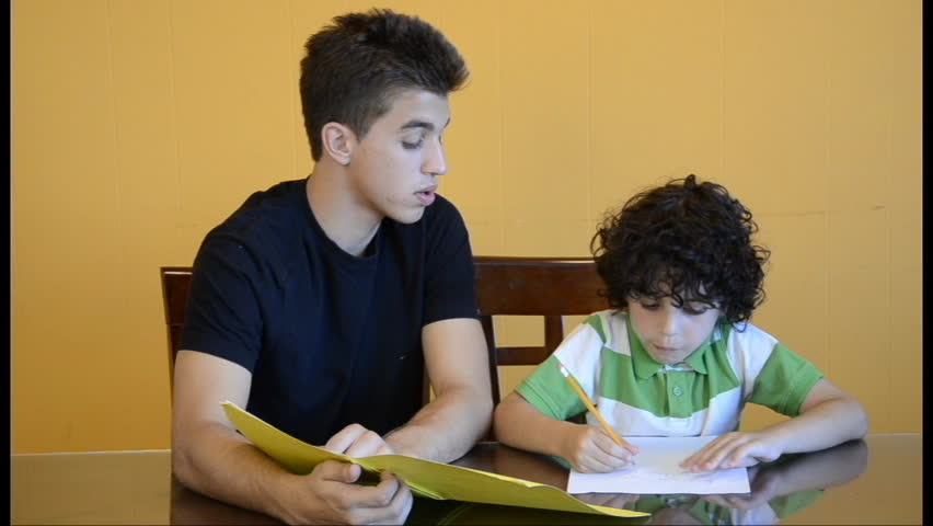 Latin boys studying together at home. Eldest son helps his brother with homework