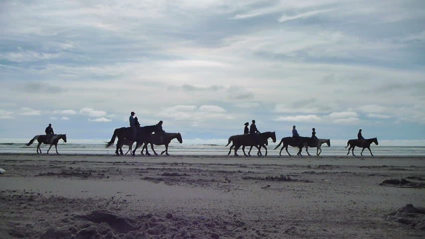 People enjoy horseback riding on sandy beach in Long Beach, Washington, real time.