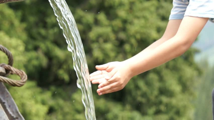 Boy refreshing his face in stream of water. Slow Motion.