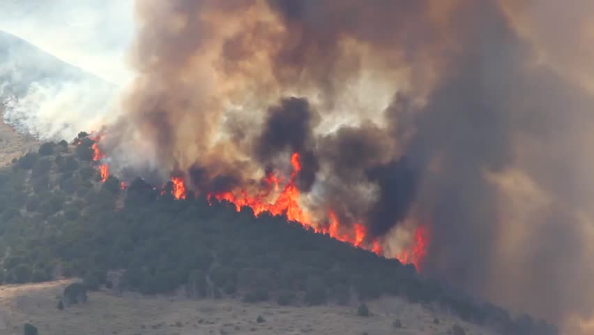A raging wildfire burns across the mountain leaving a trail of smoke and ash.
