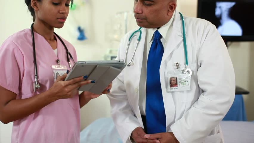 Camera tilts up to a pretty African American nurse and an Indian doctor going over what they see on an electronic tablet.