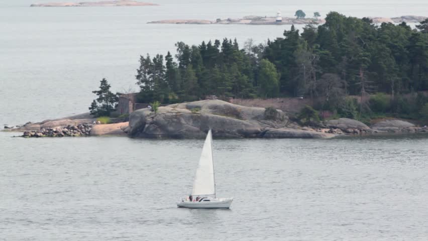 Yacht sail beside rocky coast with beacon and forest at summer day near Helsinki