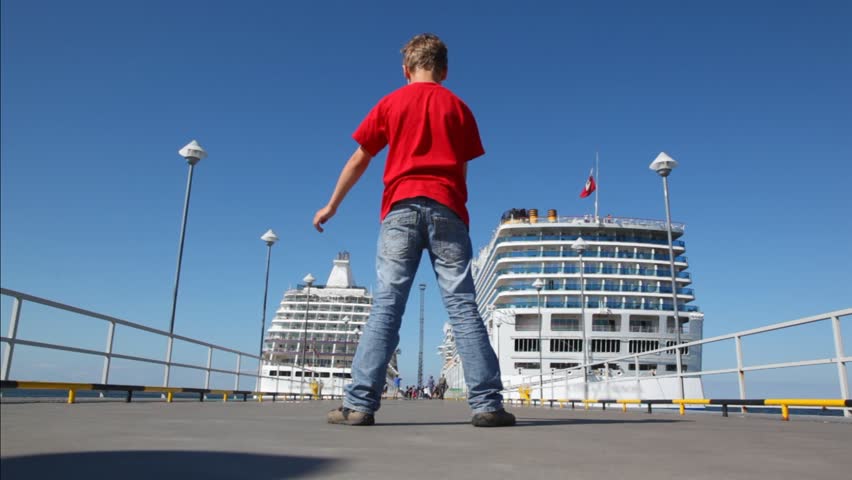 boy is turned having stretched hands on mooring at which there are two huge passenger liners