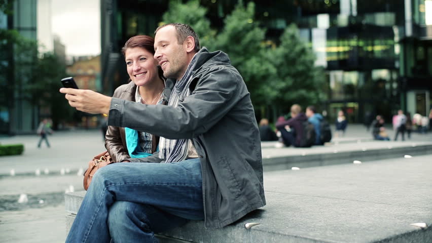 Happy couple taking photo with cellphone in the city
