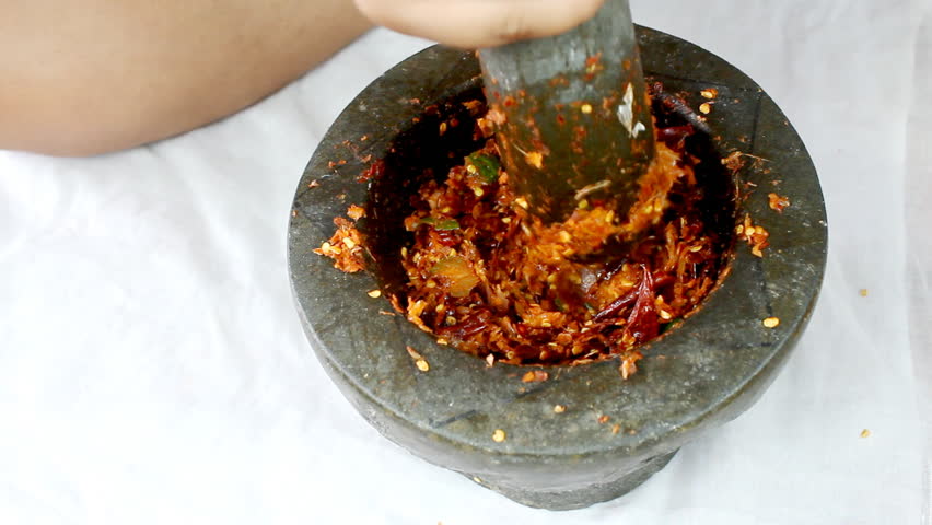 A chef is pounding dried chillies using a stone mortar