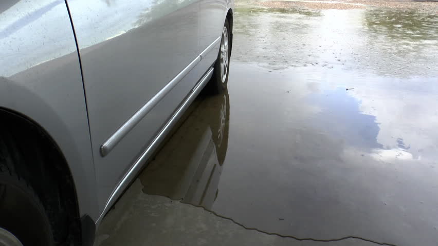 Time Lapse, Heavy rains flow around tires of parked car, engulf cement carport, as sky, raindrops reflected in puddles, car door. 
