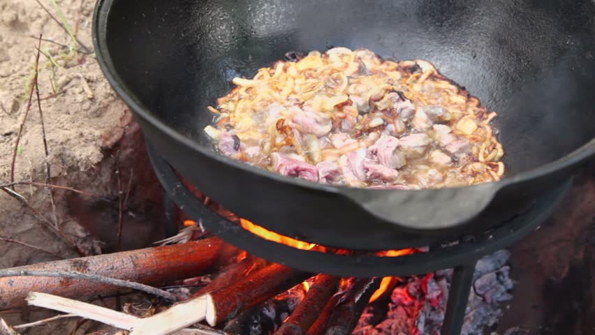 Broiled onion with meat boils in hot oil at pot on bonfire
