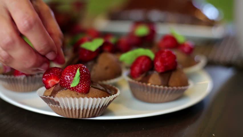 Female hands decorating chocolate muffins with strawberry
