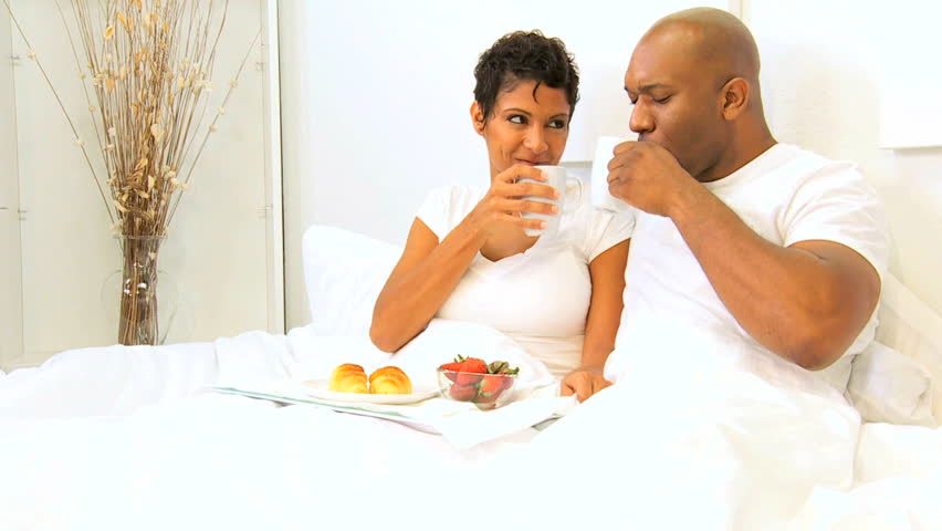 Ethnic heterosexual couple enjoying breakfast bed weekend