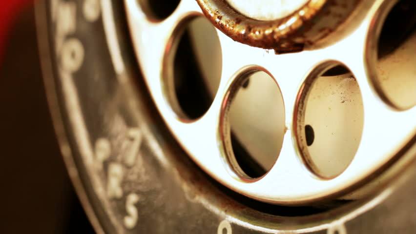 Extreme close-up of a finger dialing an old rotary pay phone.
